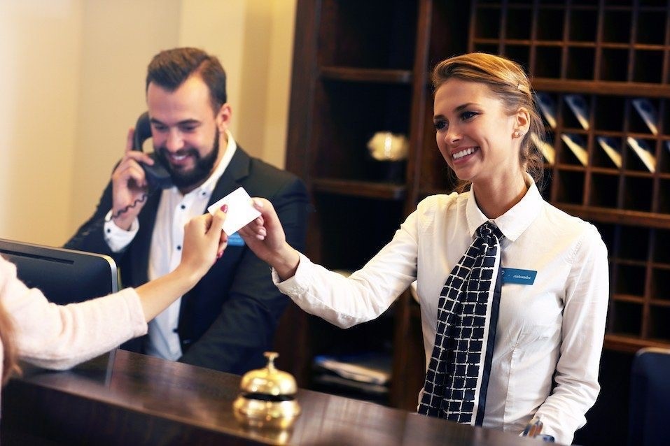 Photo dans un hotel, ou une une dame souriante de l'accueil donne une clé de chambre.