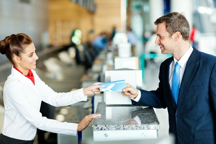 Photo dans un aéroport d'une hôtesse souriante donnant son billet d'avion à un Monsieur.